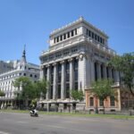 Grand buildings line a sunny street in Madrid, Spain, symbolizing urban elegance.